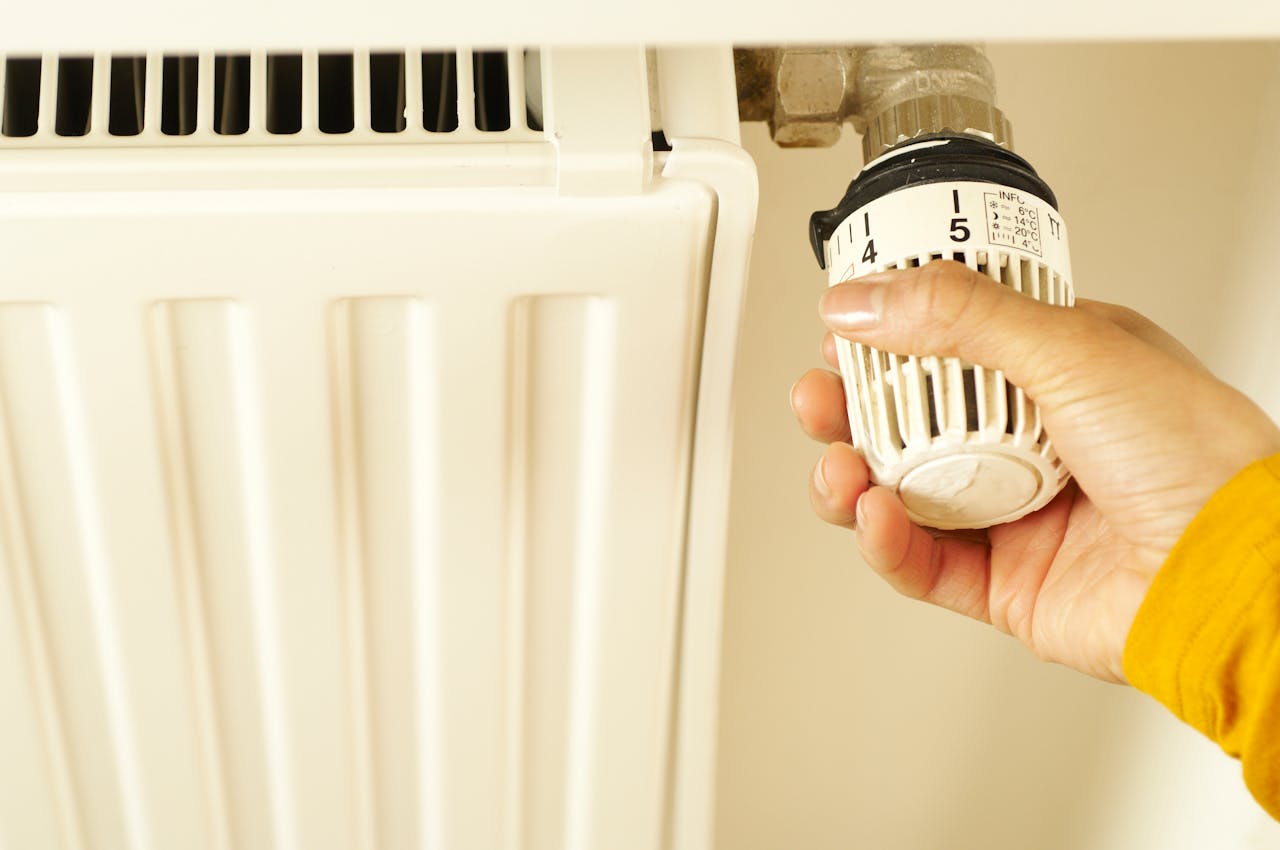 services-img-01 Close-up of hand adjusting radiator thermostat to control home heating temperature.